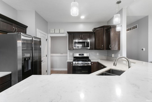 kitchen featuring stainless steel appliances, dark brown cabinets, pendant lighting, light stone countertops, and sink