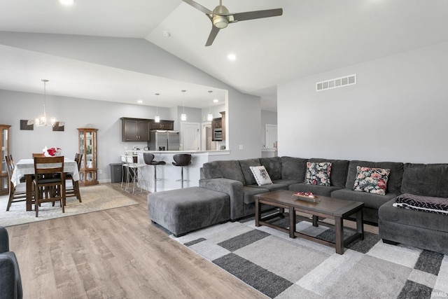 living room with light hardwood / wood-style floors, ceiling fan with notable chandelier, and high vaulted ceiling