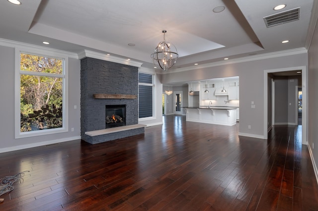 unfurnished living room with a stone fireplace, dark wood-type flooring, a notable chandelier, ornamental molding, and a tray ceiling