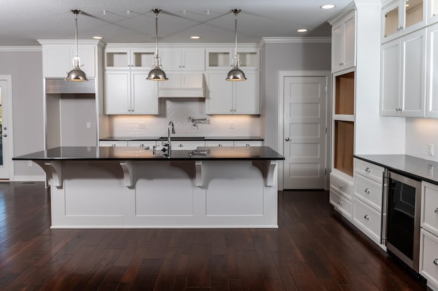 kitchen with a center island with sink, wine cooler, a kitchen breakfast bar, decorative light fixtures, and dark wood-type flooring