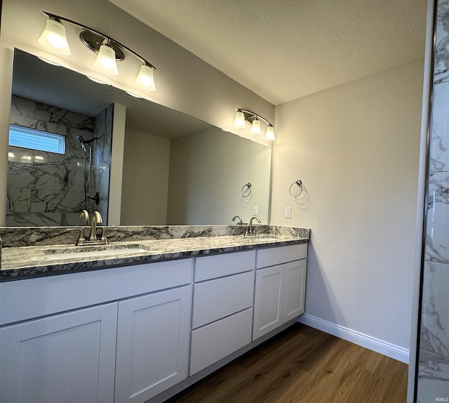 bathroom featuring a sink, a marble finish shower, wood finished floors, and double vanity