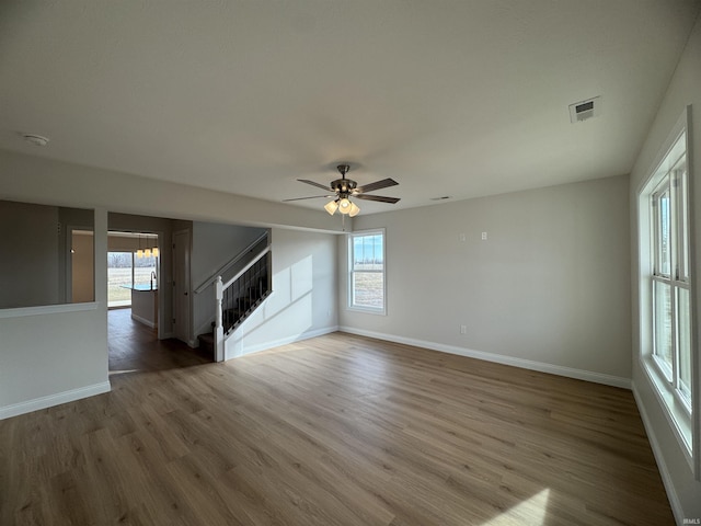 unfurnished living room featuring visible vents, baseboards, stairway, wood finished floors, and a ceiling fan