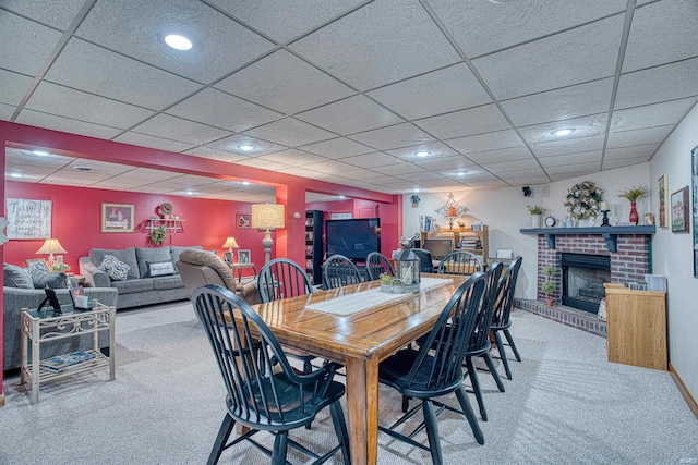 dining room with a paneled ceiling, carpet, and a brick fireplace