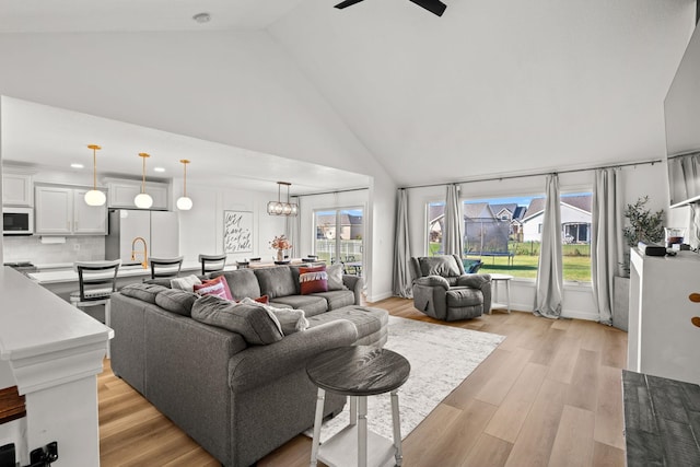 living room with light hardwood / wood-style floors, ceiling fan with notable chandelier, a healthy amount of sunlight, and high vaulted ceiling