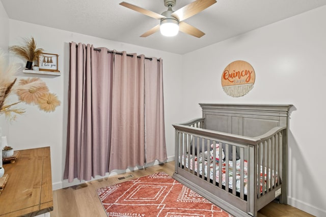 bedroom with a nursery area, hardwood / wood-style flooring, and ceiling fan