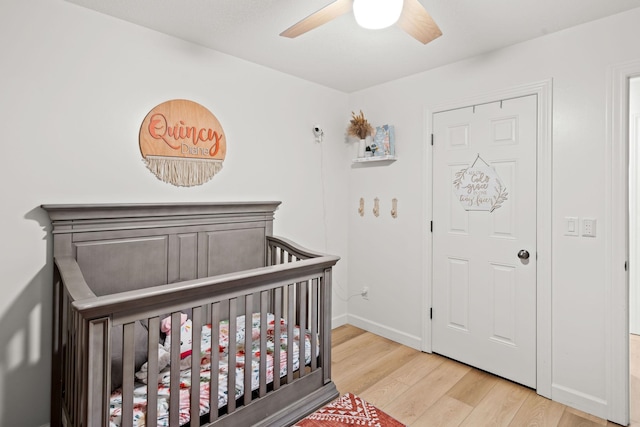 bedroom with a crib, light hardwood / wood-style flooring, and ceiling fan