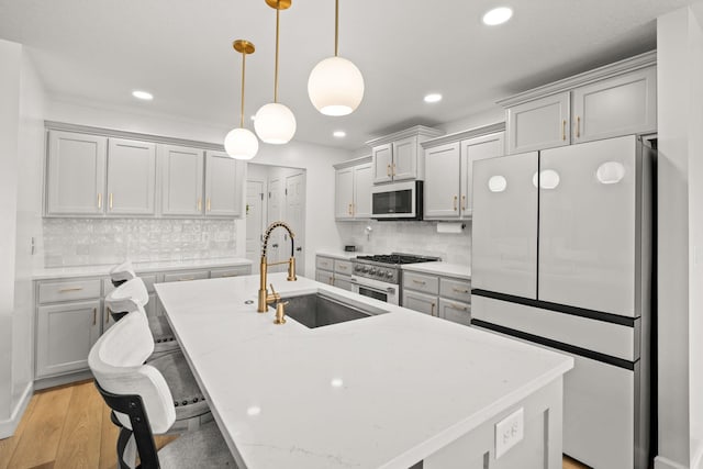 kitchen featuring decorative backsplash, sink, an island with sink, appliances with stainless steel finishes, and decorative light fixtures