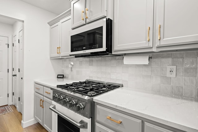 kitchen featuring appliances with stainless steel finishes, decorative backsplash, light stone counters, and light hardwood / wood-style flooring