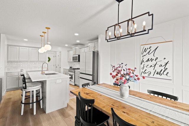 kitchen featuring a center island with sink, stainless steel appliances, hanging light fixtures, sink, and light hardwood / wood-style flooring