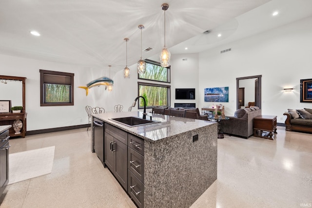 kitchen featuring light stone counters, a towering ceiling, hanging light fixtures, sink, and an island with sink