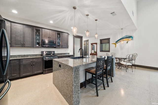 kitchen featuring stainless steel appliances, sink, an island with sink, stone countertops, and decorative light fixtures