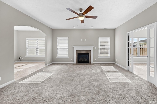 unfurnished living room with ceiling fan, a healthy amount of sunlight, light carpet, and a textured ceiling