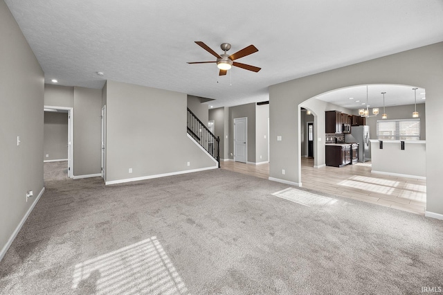 unfurnished living room featuring ceiling fan with notable chandelier, light colored carpet, and a textured ceiling