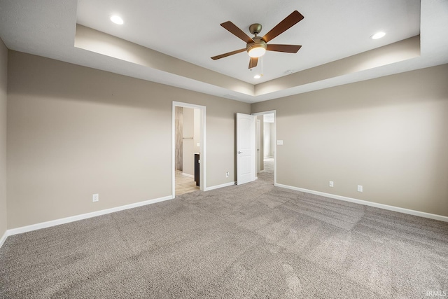 empty room with ceiling fan, light carpet, and a tray ceiling