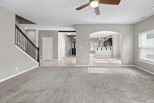 unfurnished living room featuring a textured ceiling, light carpet, and ceiling fan with notable chandelier