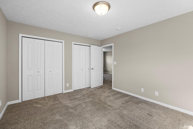 unfurnished bedroom featuring multiple closets, carpet floors, and a textured ceiling