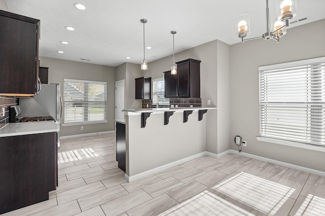 kitchen with dark brown cabinets, a notable chandelier, hanging light fixtures, a breakfast bar area, and kitchen peninsula