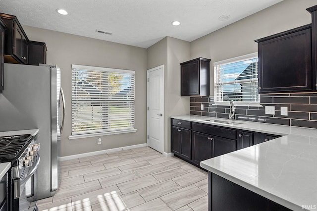 kitchen with decorative backsplash, stainless steel stove, sink, and a textured ceiling