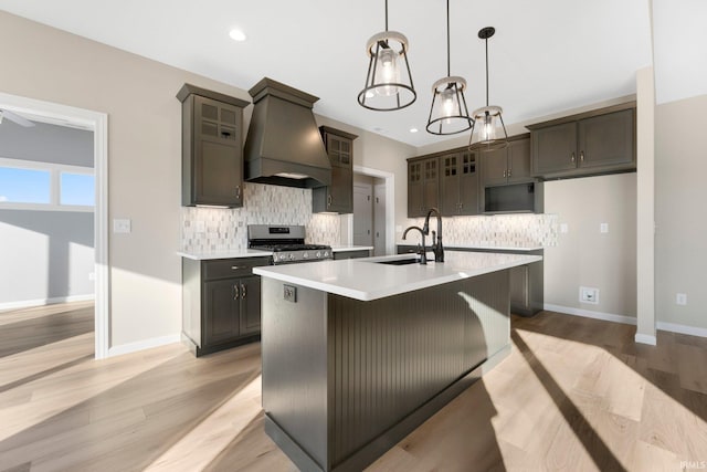 kitchen featuring sink, dark brown cabinets, an island with sink, custom range hood, and stainless steel range oven