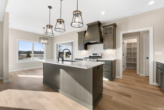 kitchen featuring pendant lighting, stainless steel stove, sink, a kitchen island with sink, and custom range hood