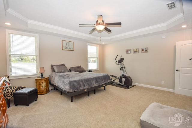 bedroom with light colored carpet, a tray ceiling, multiple windows, and ceiling fan