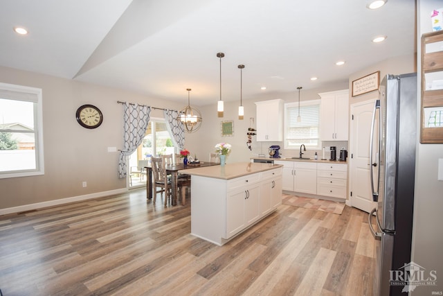 kitchen featuring white cabinets, decorative light fixtures, stainless steel refrigerator, and a center island