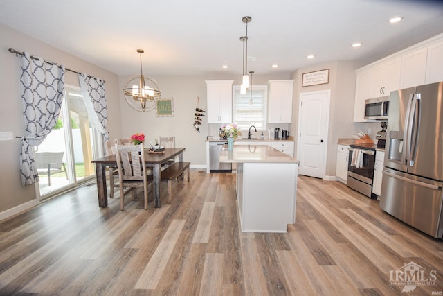 kitchen with appliances with stainless steel finishes, decorative light fixtures, light hardwood / wood-style flooring, a kitchen island, and white cabinets