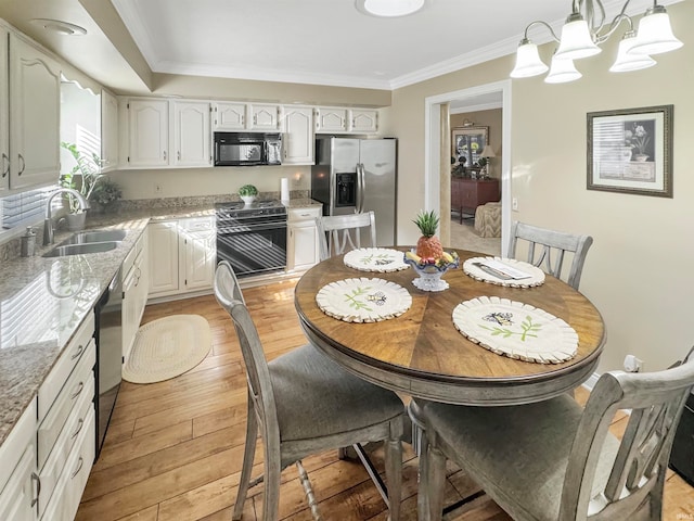 kitchen featuring black appliances, light stone counters, decorative light fixtures, sink, and light hardwood / wood-style flooring