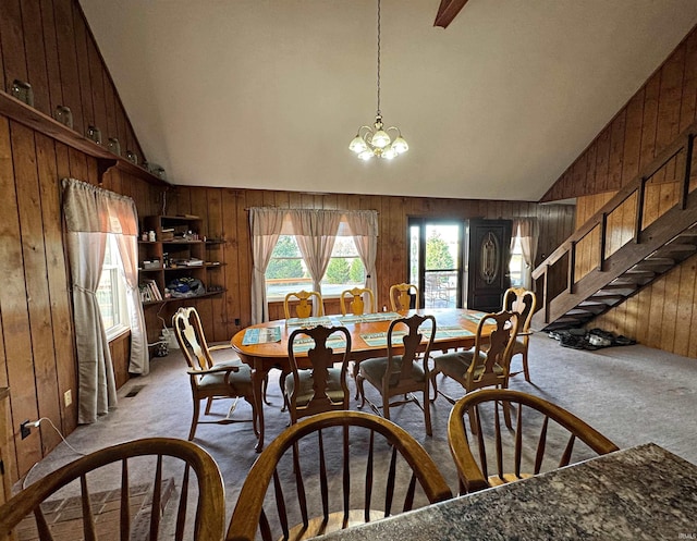 dining room with wood walls, high vaulted ceiling, a notable chandelier, and light carpet