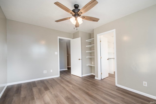 unfurnished bedroom featuring a spacious closet, wood-type flooring, ceiling fan, and a closet