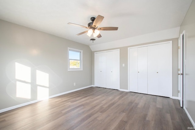 unfurnished bedroom featuring multiple closets, wood-type flooring, and ceiling fan