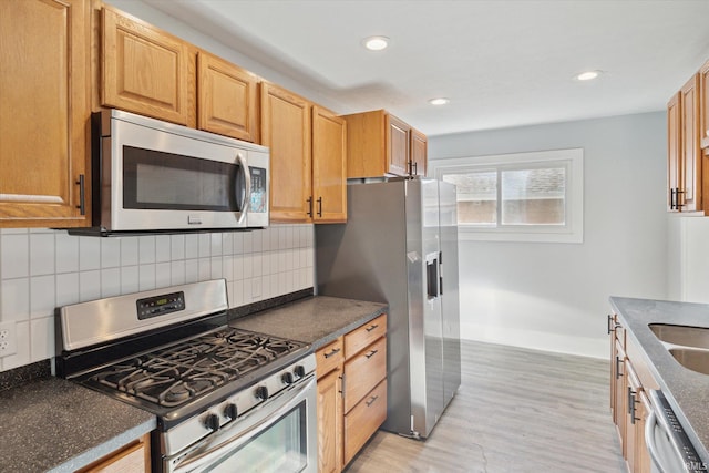 kitchen with appliances with stainless steel finishes, sink, tasteful backsplash, and light hardwood / wood-style flooring