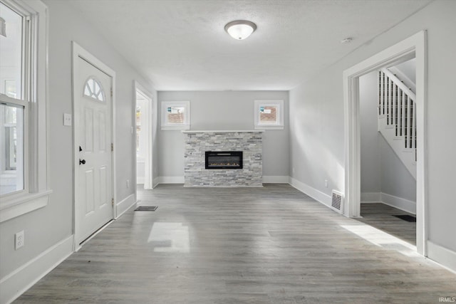 unfurnished living room with a stone fireplace, a textured ceiling, and hardwood / wood-style flooring