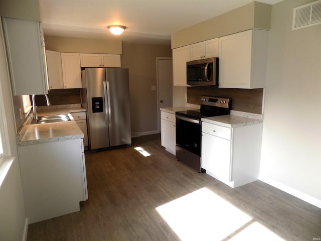 kitchen with dark hardwood / wood-style flooring, white cabinets, decorative backsplash, and stainless steel appliances