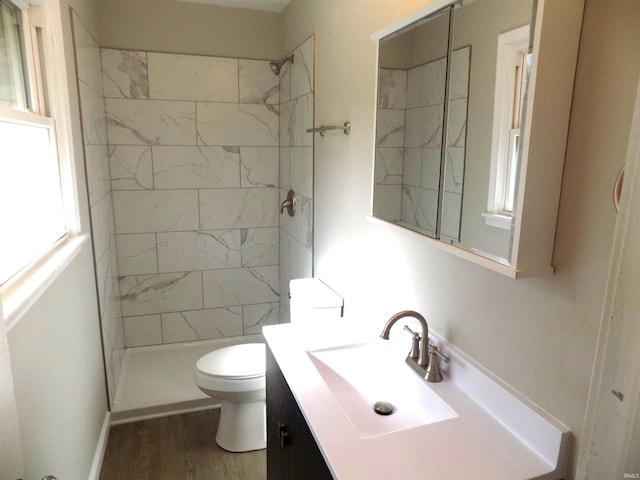 bathroom with hardwood / wood-style floors, vanity, toilet, and a tile shower