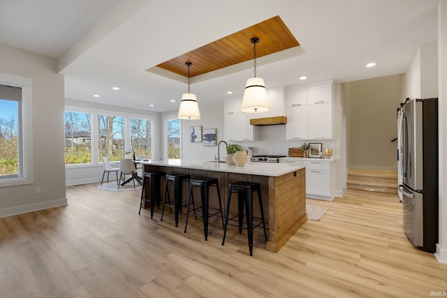 kitchen featuring white cabinets, light hardwood / wood-style flooring, an island with sink, pendant lighting, and appliances with stainless steel finishes