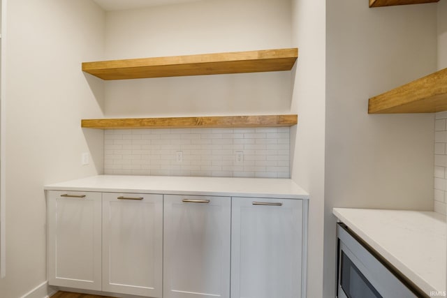 bar with white cabinets, stainless steel microwave, tasteful backsplash, and light stone countertops