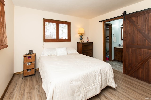 bedroom featuring connected bathroom, light wood-type flooring, and a barn door