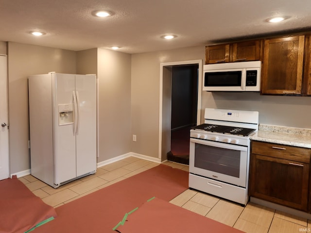 kitchen with white appliances, a textured ceiling, dark brown cabinets, and light tile patterned flooring