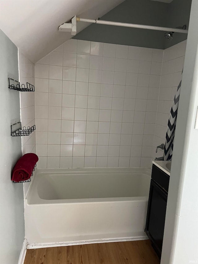 bathroom with tiled shower / bath combo, vanity, hardwood / wood-style floors, and vaulted ceiling