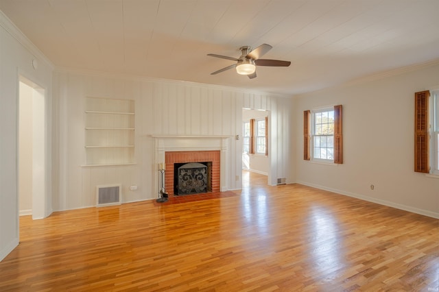 unfurnished living room with built in shelves, ornamental molding, a fireplace, ceiling fan, and light hardwood / wood-style flooring