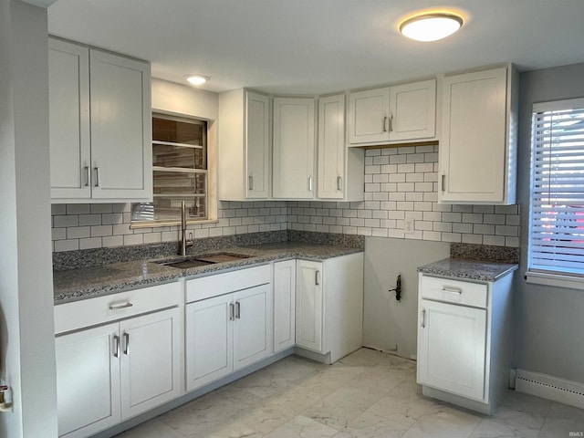 kitchen with a baseboard heating unit, sink, backsplash, white cabinetry, and dark stone countertops