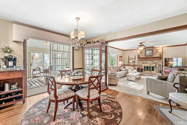 dining room featuring ceiling fan with notable chandelier, light hardwood / wood-style floors, a textured ceiling, ornamental molding, and a fireplace