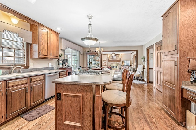 kitchen with stainless steel appliances, a kitchen island, hanging light fixtures, light hardwood / wood-style floors, and a brick fireplace