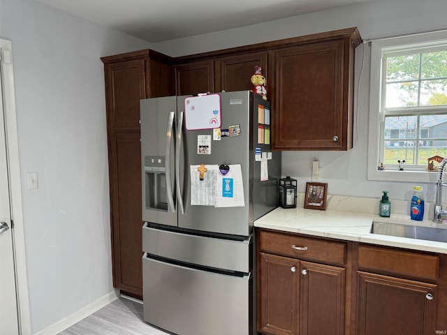 kitchen with light hardwood / wood-style floors, light stone counters, stainless steel refrigerator with ice dispenser, dark brown cabinetry, and sink