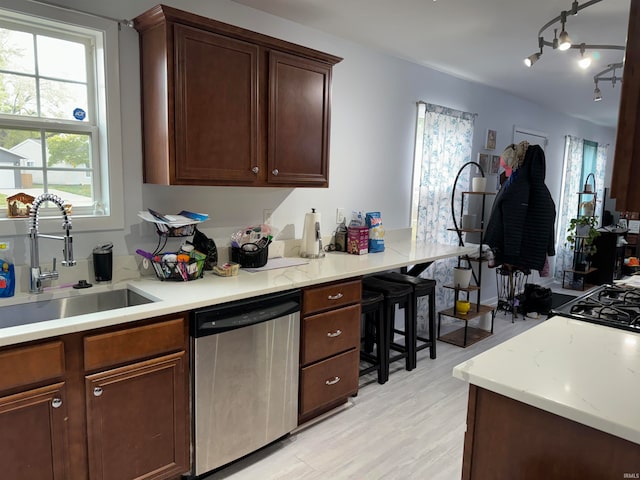 kitchen featuring light hardwood / wood-style floors, sink, light stone countertops, stainless steel dishwasher, and dark brown cabinets