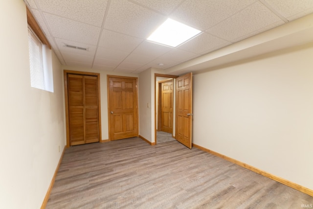 unfurnished bedroom with a drop ceiling, light hardwood / wood-style flooring, and a closet