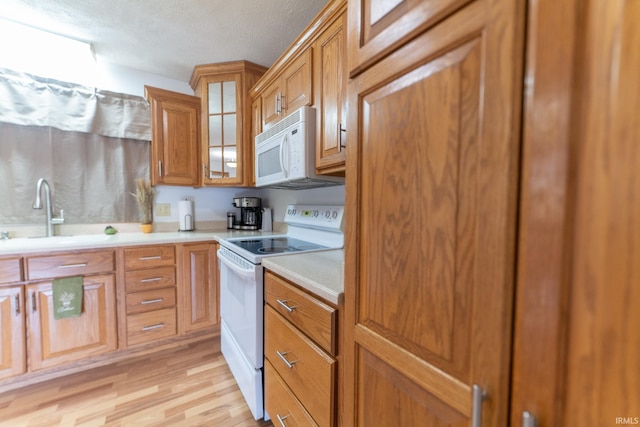 kitchen with white appliances, a textured ceiling, sink, and light hardwood / wood-style flooring