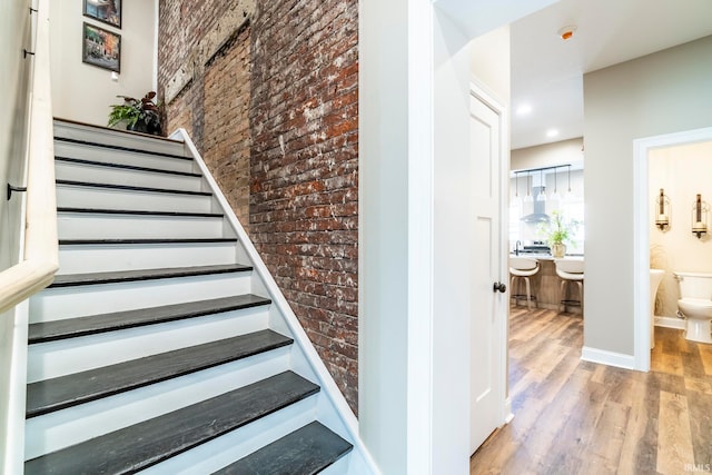 stairway with brick wall and hardwood / wood-style flooring