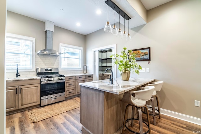 kitchen with stainless steel range with gas stovetop, sink, a kitchen breakfast bar, hanging light fixtures, and wall chimney range hood